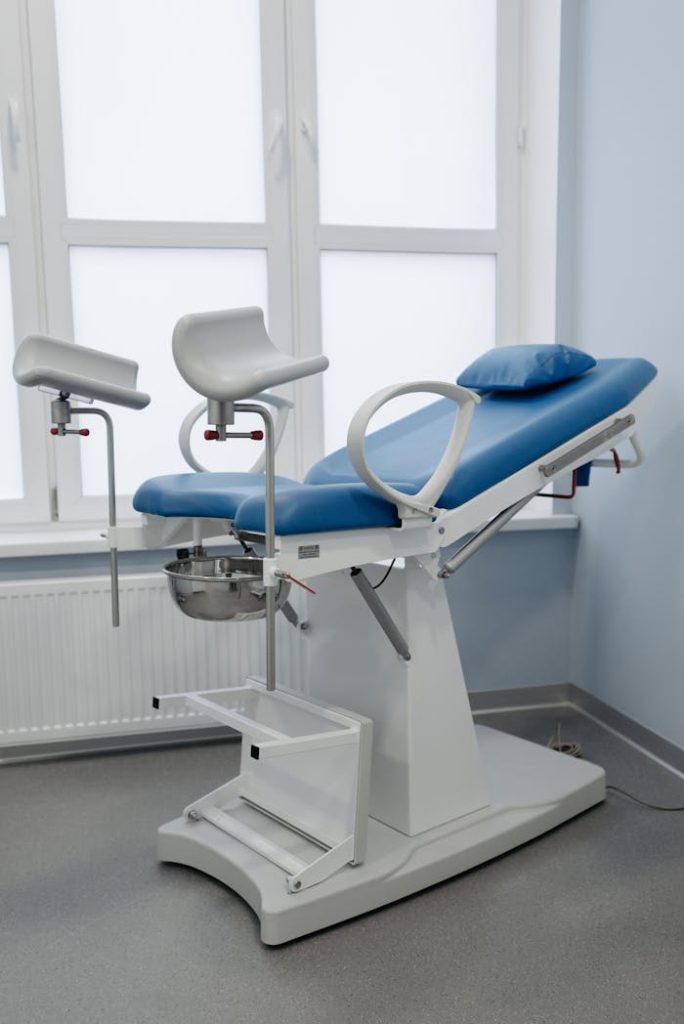 a-blue-gynecological-chair-7108121 A modern gynecological chair in a sterile medical facility, featuring adjustable armrests and clean design.
